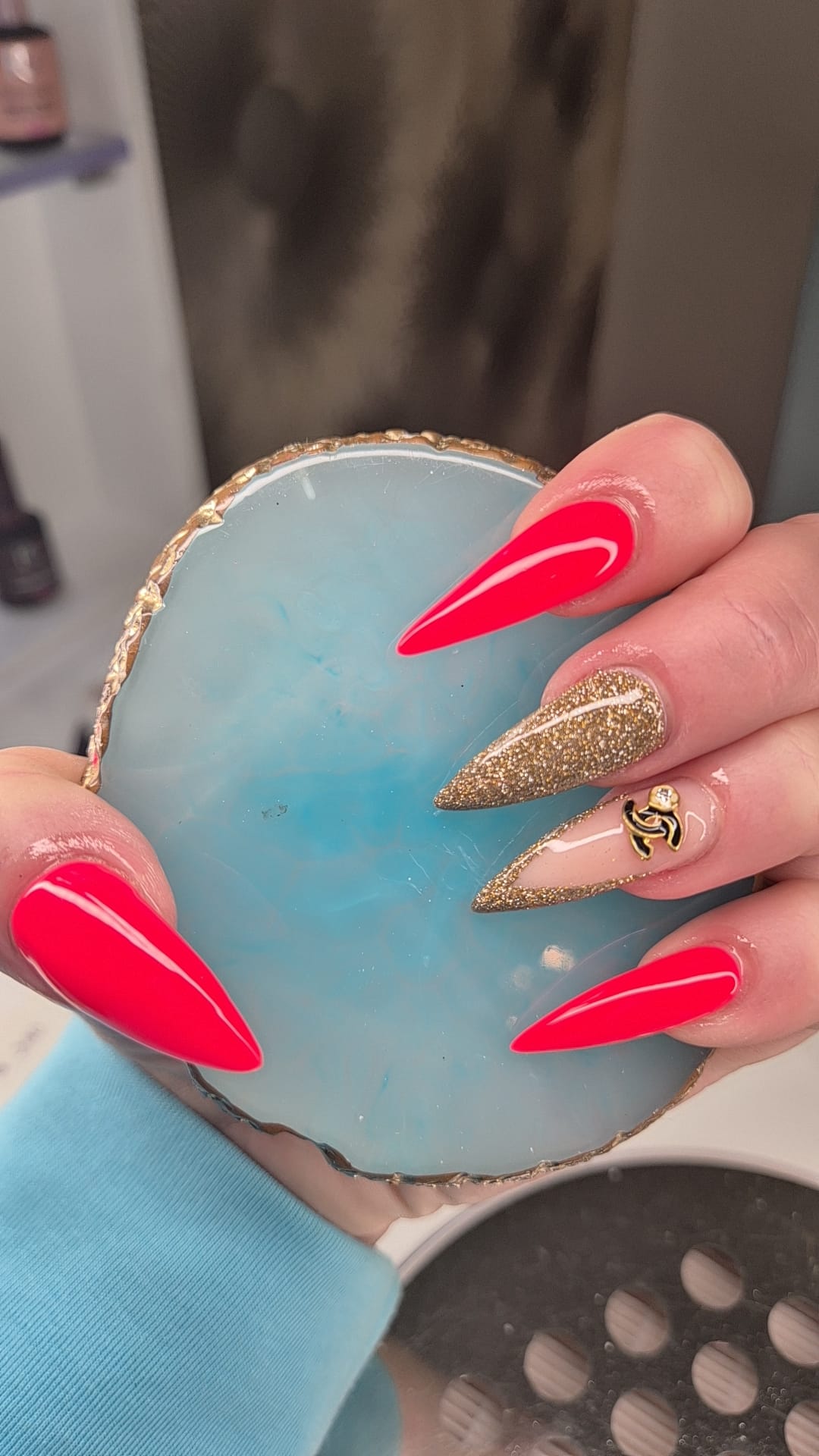 Felrode stiletto nagels met goudglitter boven een blauwe agaatschaal