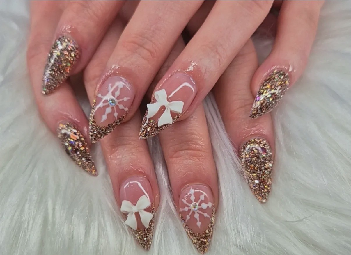 Stiletto nagels met goudglitter, French tips, witte strikjes en sneeuwvlokjes op een witte vacht